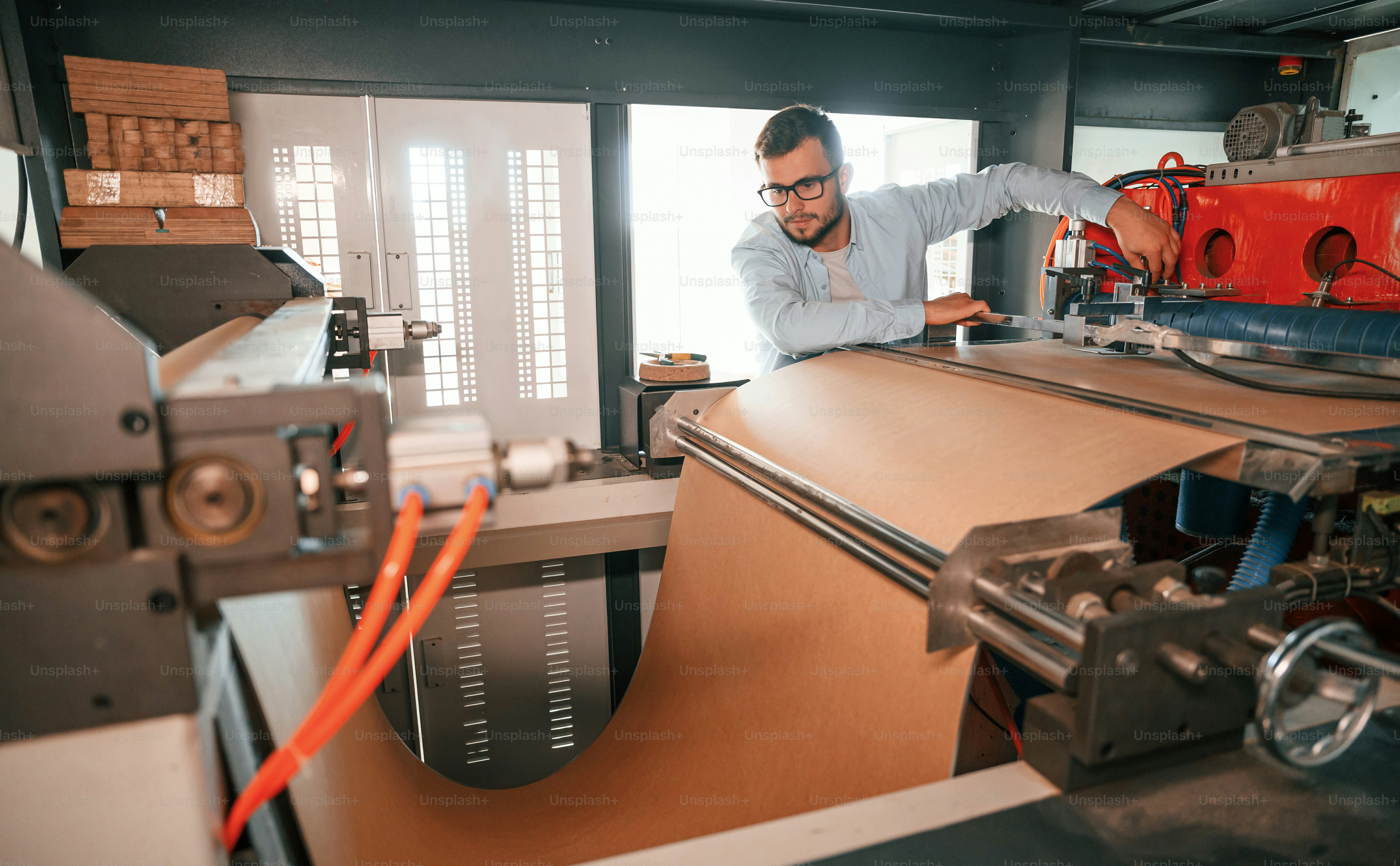 Sheet cutting machine. Operating device. Print house worker in white clothes is indoors.