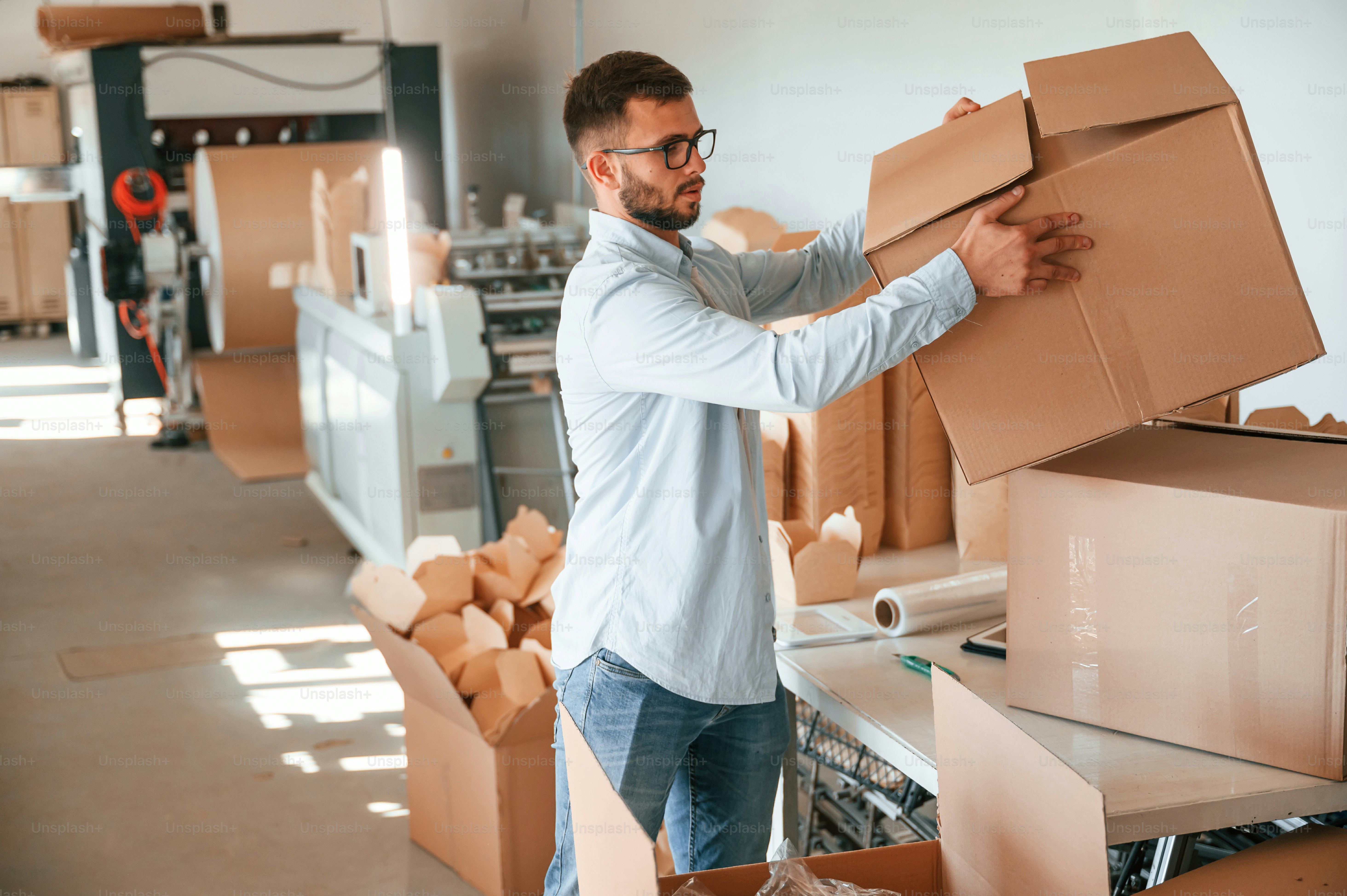 Moving the boxes with raw material. Print house worker in white clothes is indoors.