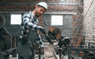 Working by operating machine. Factory worker in uniform is indoors.