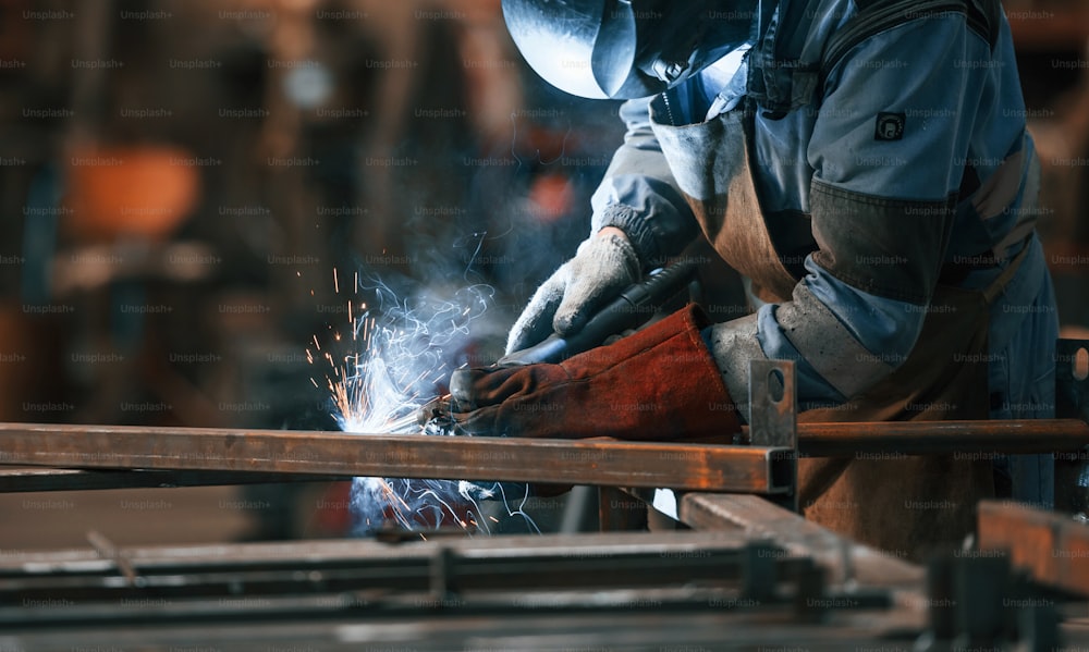 Close up view. Factory worker in protective mask is welding the iron.