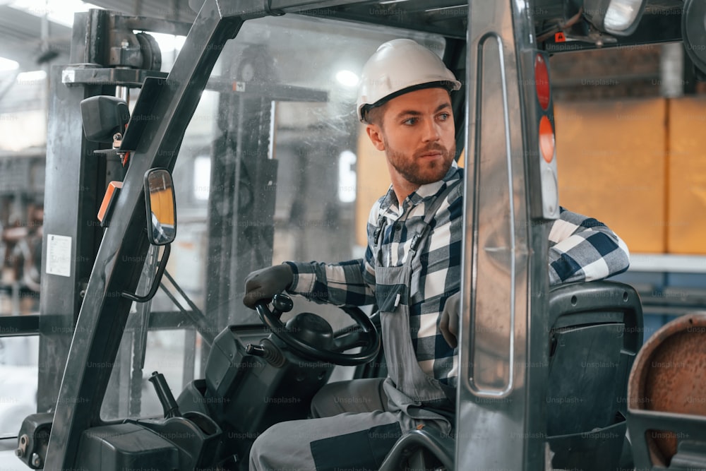 In forklift. Factory male worker in uniform is indoors.