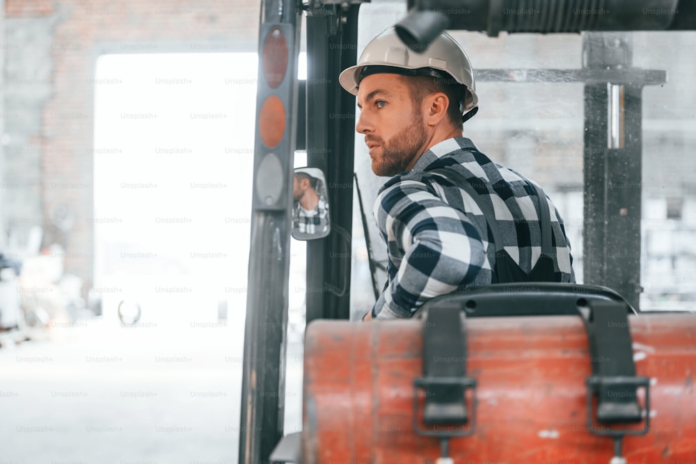 In forklift. Factory male worker in uniform is indoors.