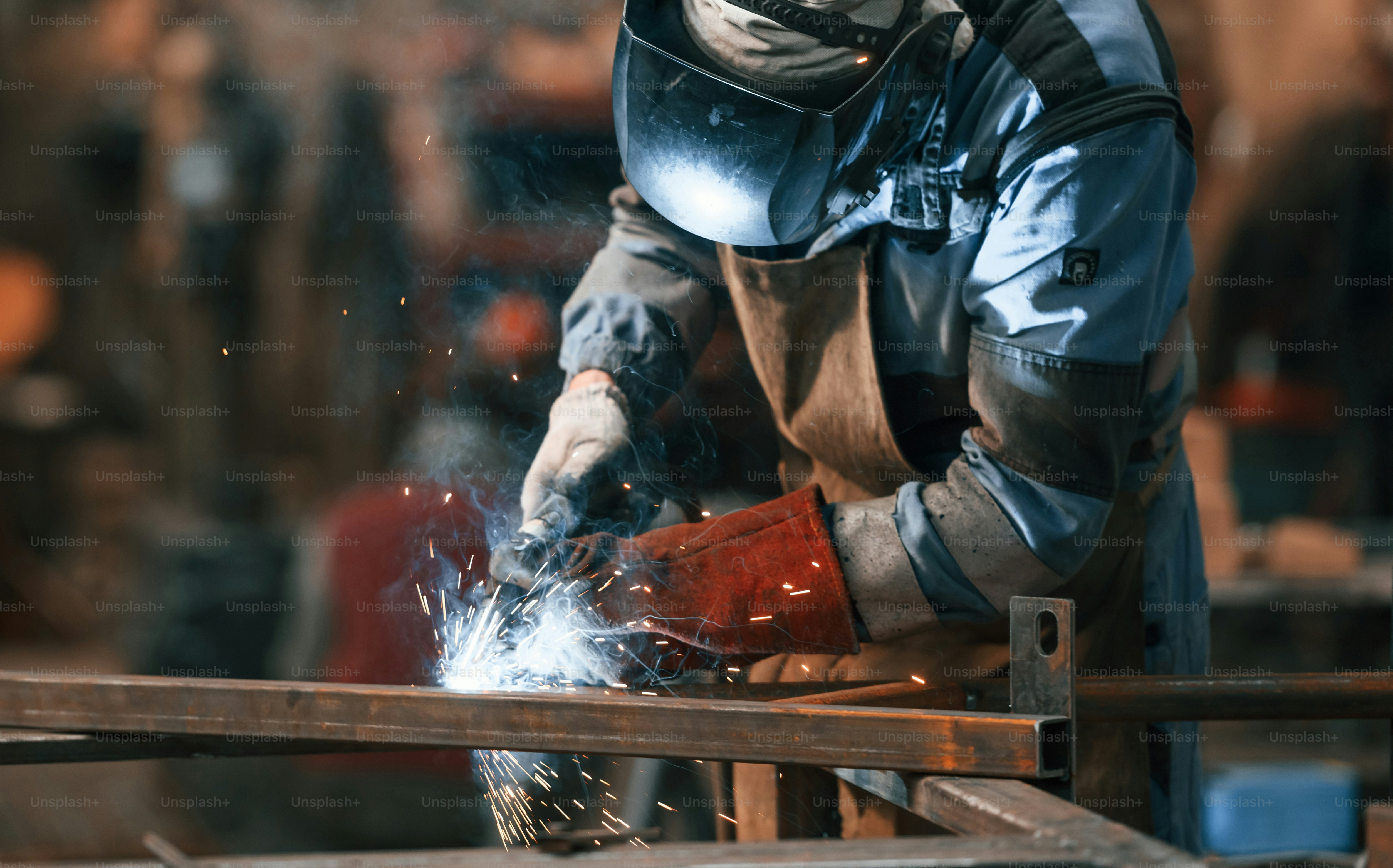 接写図。保護マスクを着た工場労働者がアイロンを溶接しています。