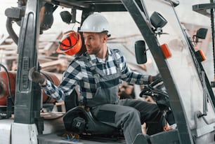 Driving the vehicle. Factory male worker in uniform is indoors.