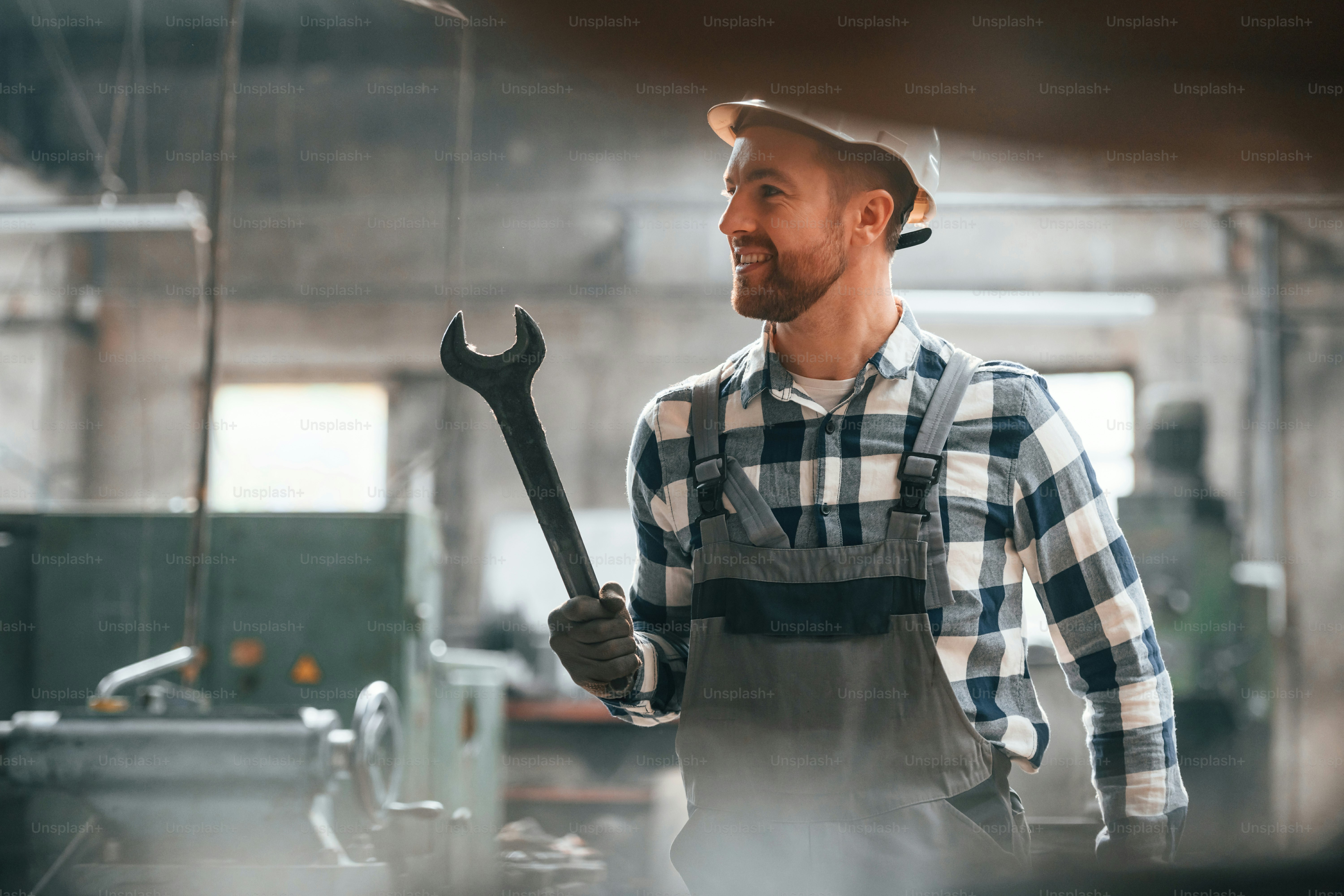 レンチを手に。制服を着た工場の男性労働者は屋内にいる。