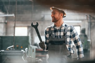 With wrench in hand. Factory male worker in uniform is indoors.