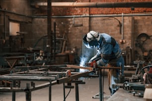 Factory worker in protective mask is welding the iron.