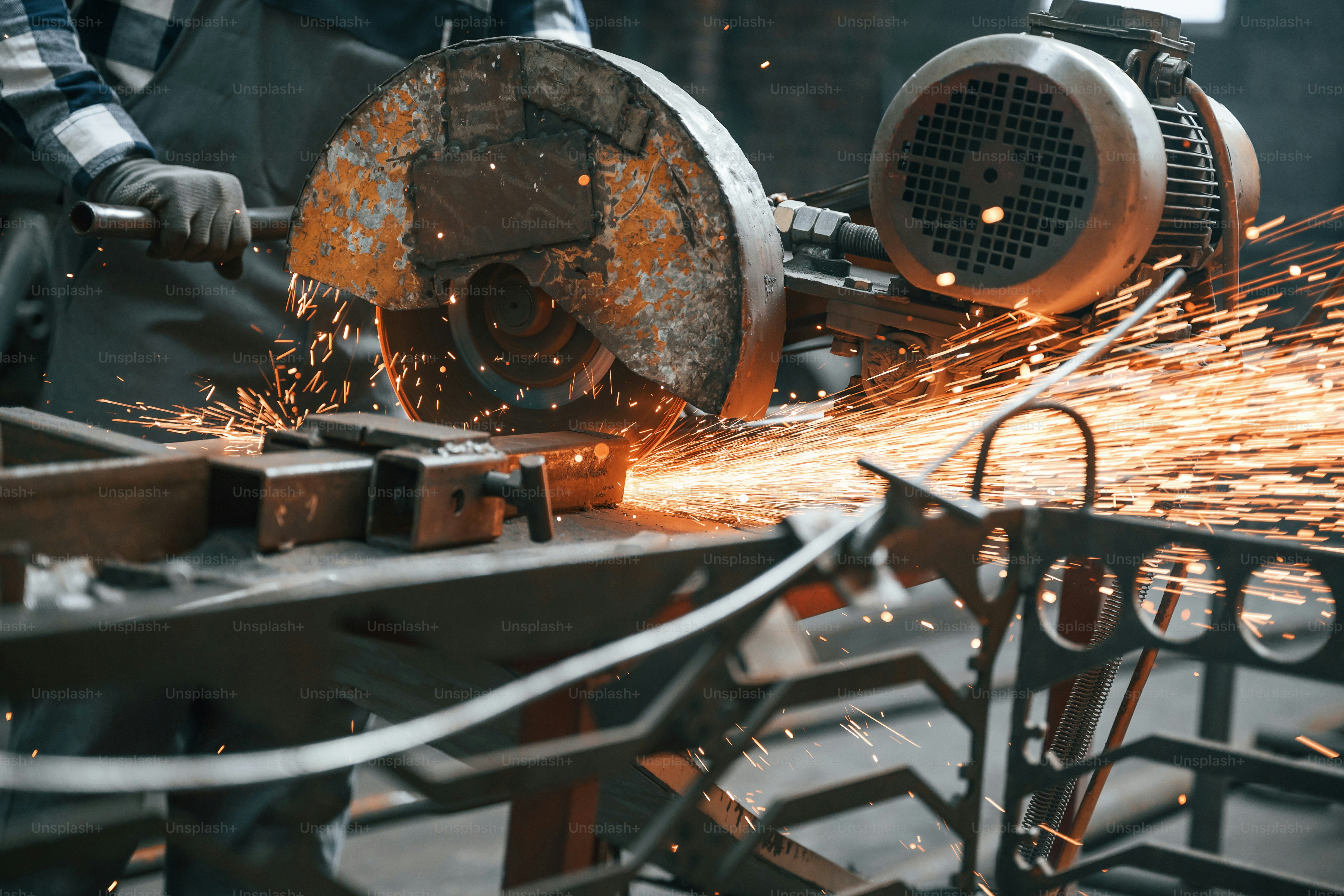 Many of the sparks. Cutting metal. Factory male worker in uniform is indoors.