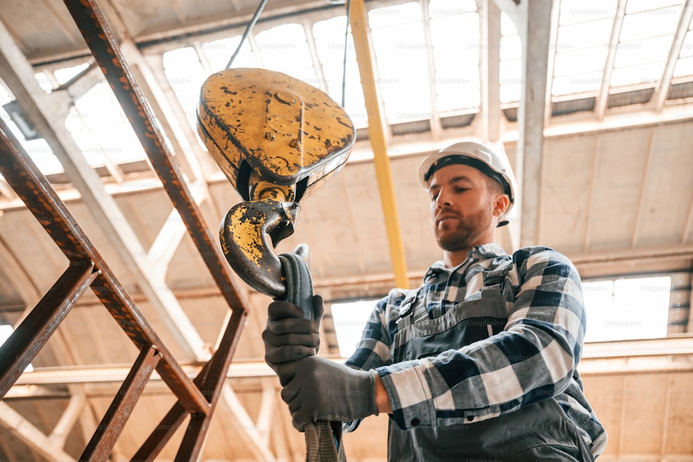 Working with crane. Man in a factory in uniform is indoors.