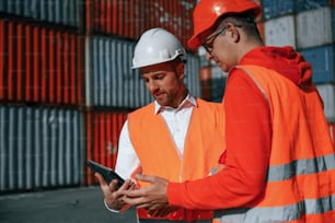Using digital tablet. Two male workers is on the location with containers.