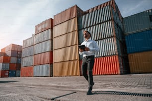 Controlling the process. Holding digital tablet. Male worker is on the location with containers.