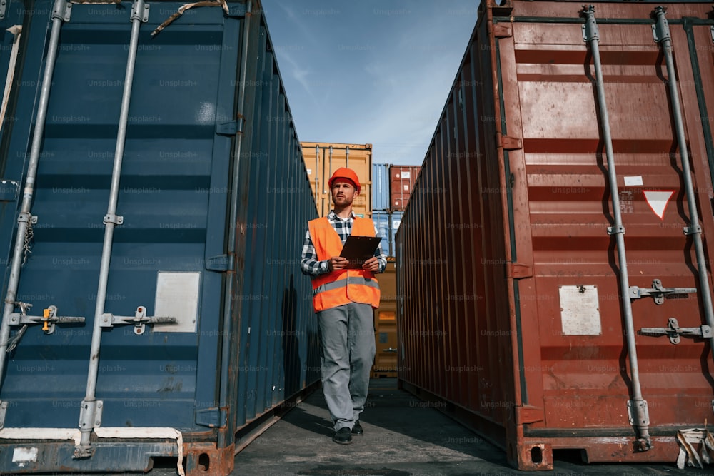 Male worker is on the location with containers. Using digital tablet.