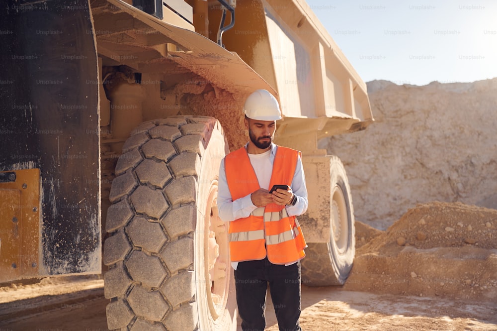 Using smartphone. Man in uniform is working in the quarry at daytime.