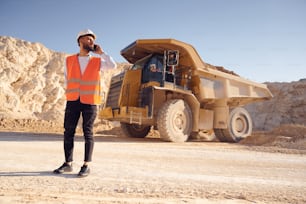 Using smartphone. Man in uniform is working in the quarry at daytime.