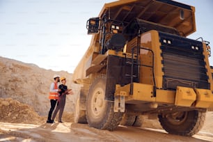 Looking at big haul truck. Two men in uniform are working together in the quarry.