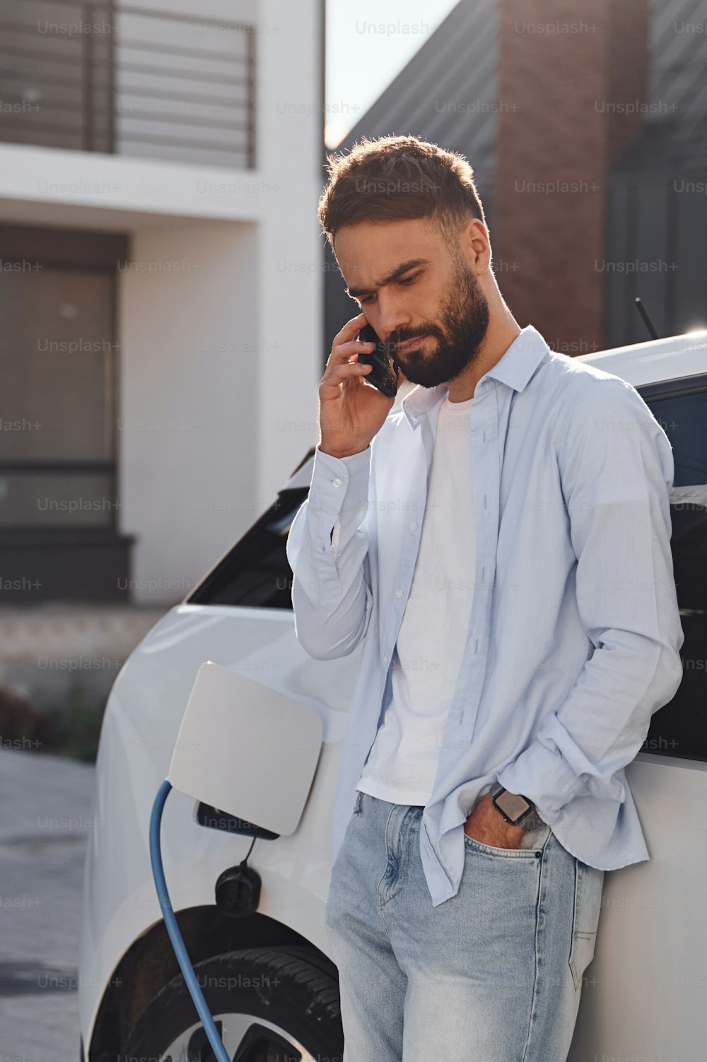 Talking by the phone. Young stylish man is with electric car at daytime.