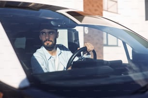 Sitting in the vehicle. Young stylish man is with electric car at daytime.