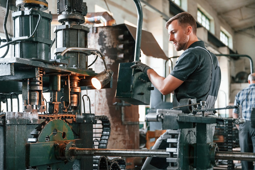 Standing by metal processing device. Man in uniform is in workstation developing details of agriculture technique.