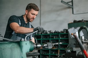 Working with metal. Man in uniform is indoors developing details of agriculture technique.