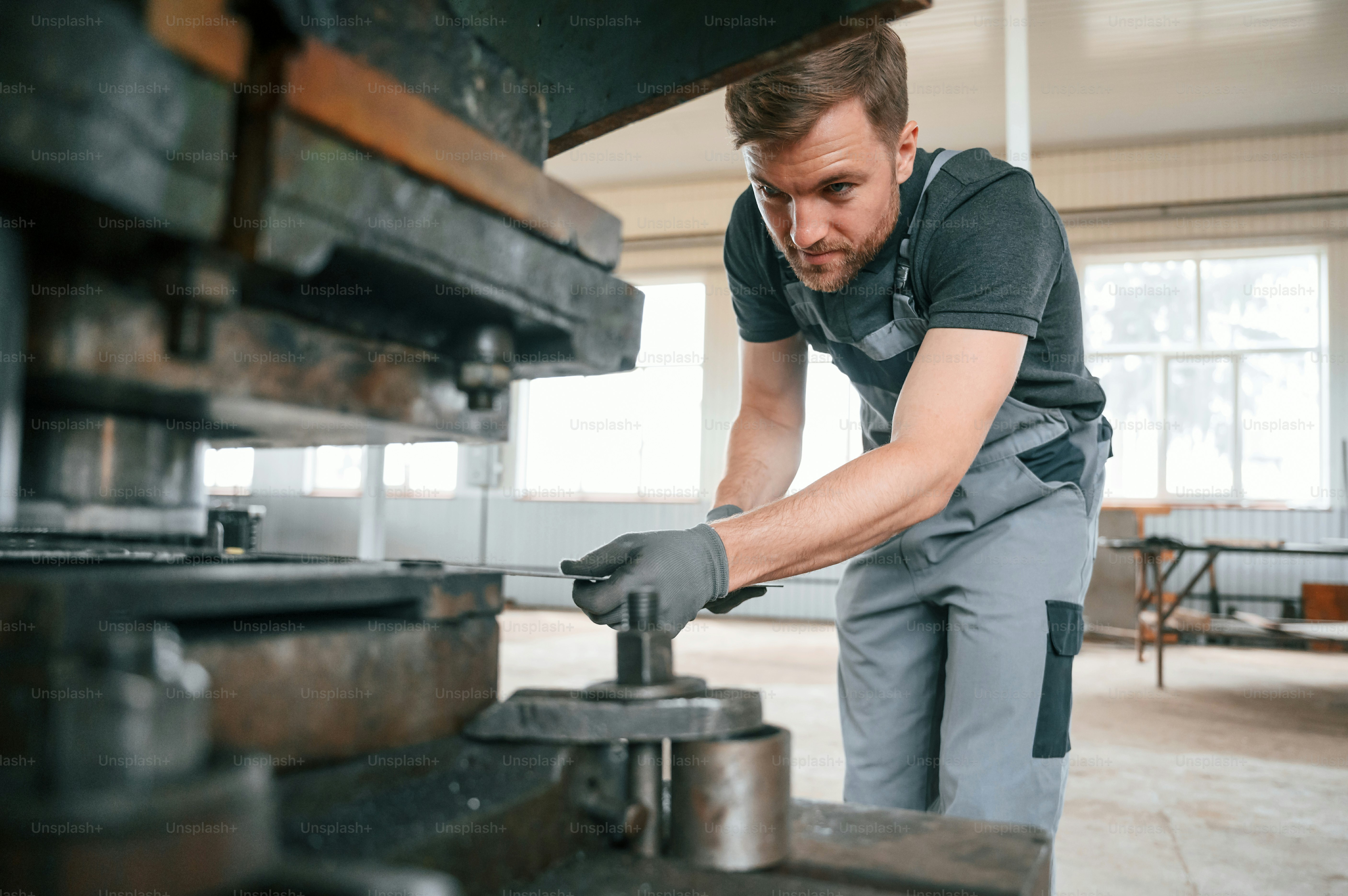 Operando equipamentos de fabricação. Homem de uniforme está em estação de trabalho desenvolvendo detalhes da técnica agrícola.