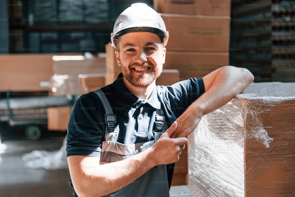 Leaning on the box and smiling. Employee in uniform is working in the storage at daytime.