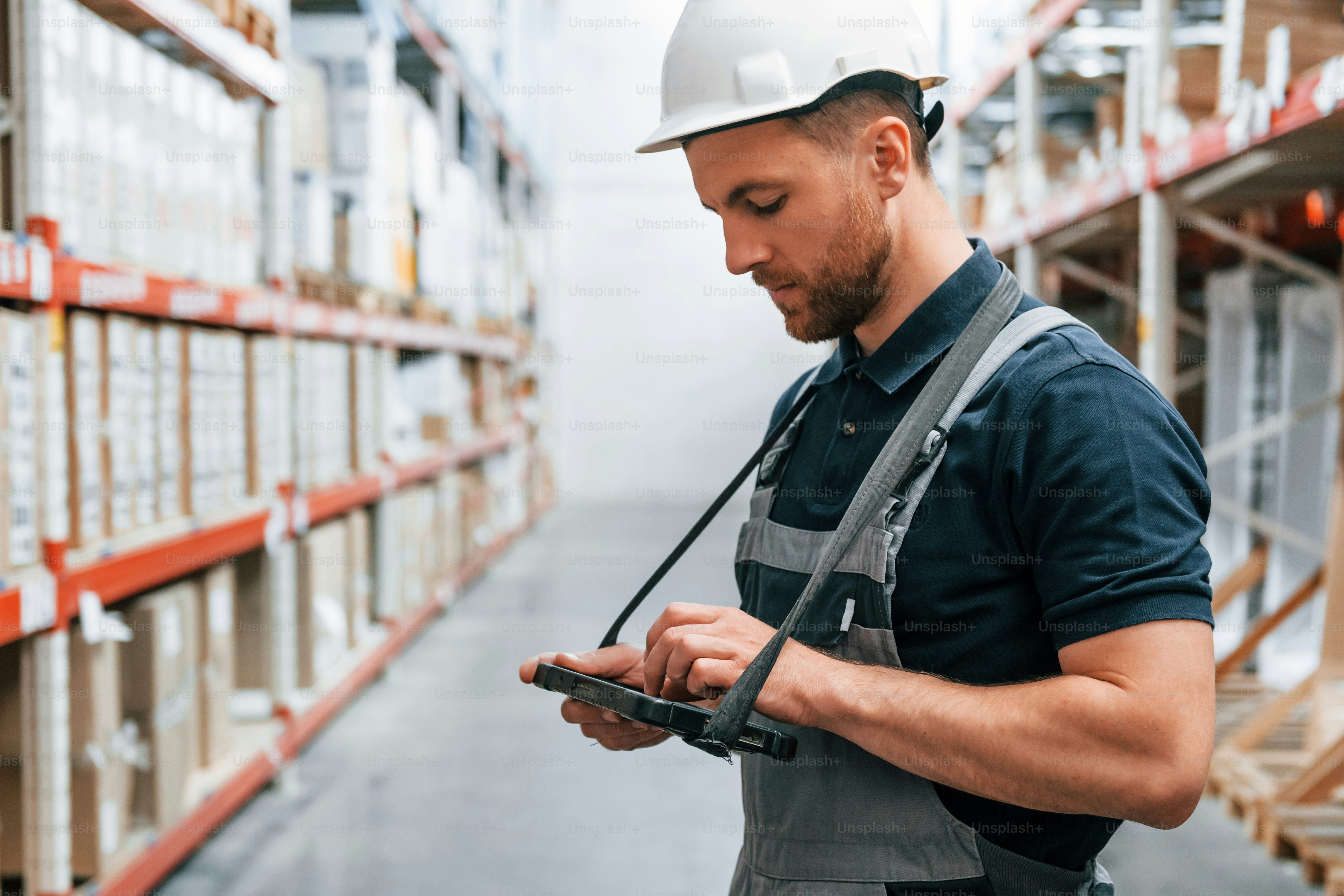 Checking data in the tablet. Employee in uniform is working in the storage at daytime.