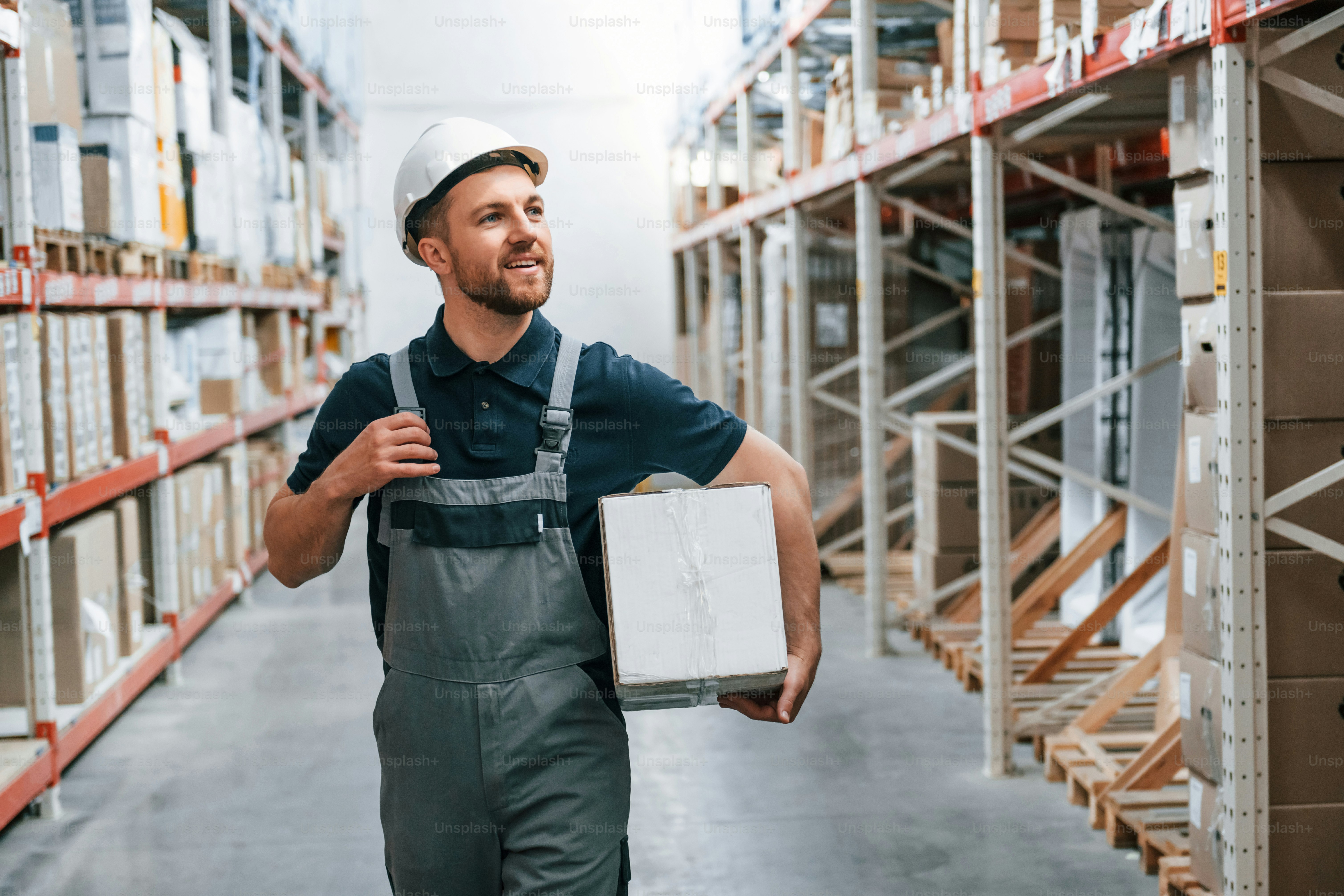 With delivery package in hands. Employee in uniform is working in the storage at daytime.