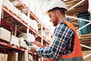 With tablet. Employee in uniform is working in the storage at daytime.