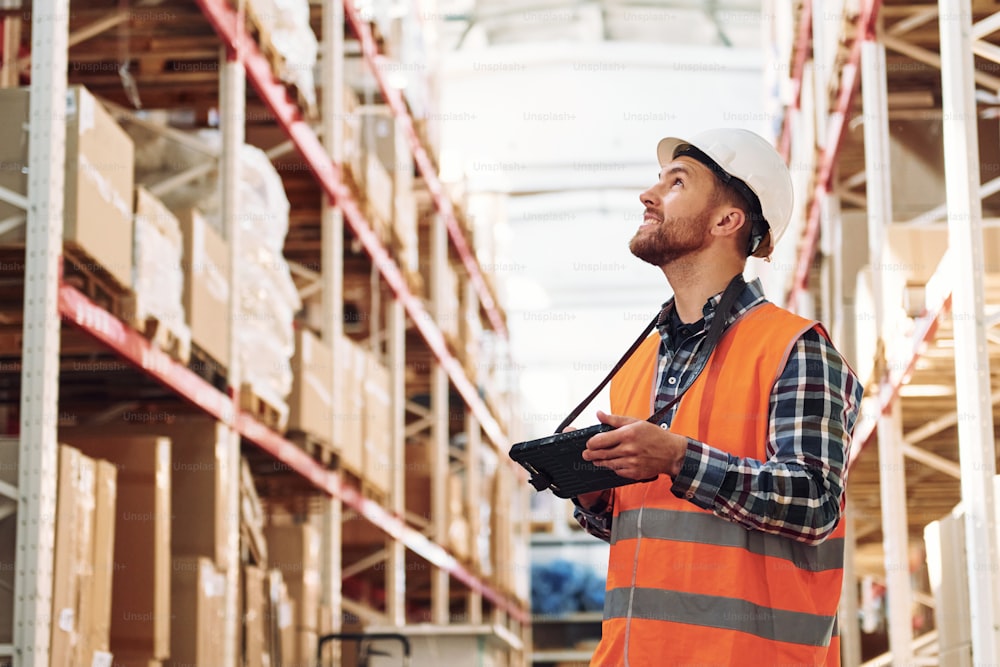 With tablet. Employee in uniform is working in the storage at daytime.