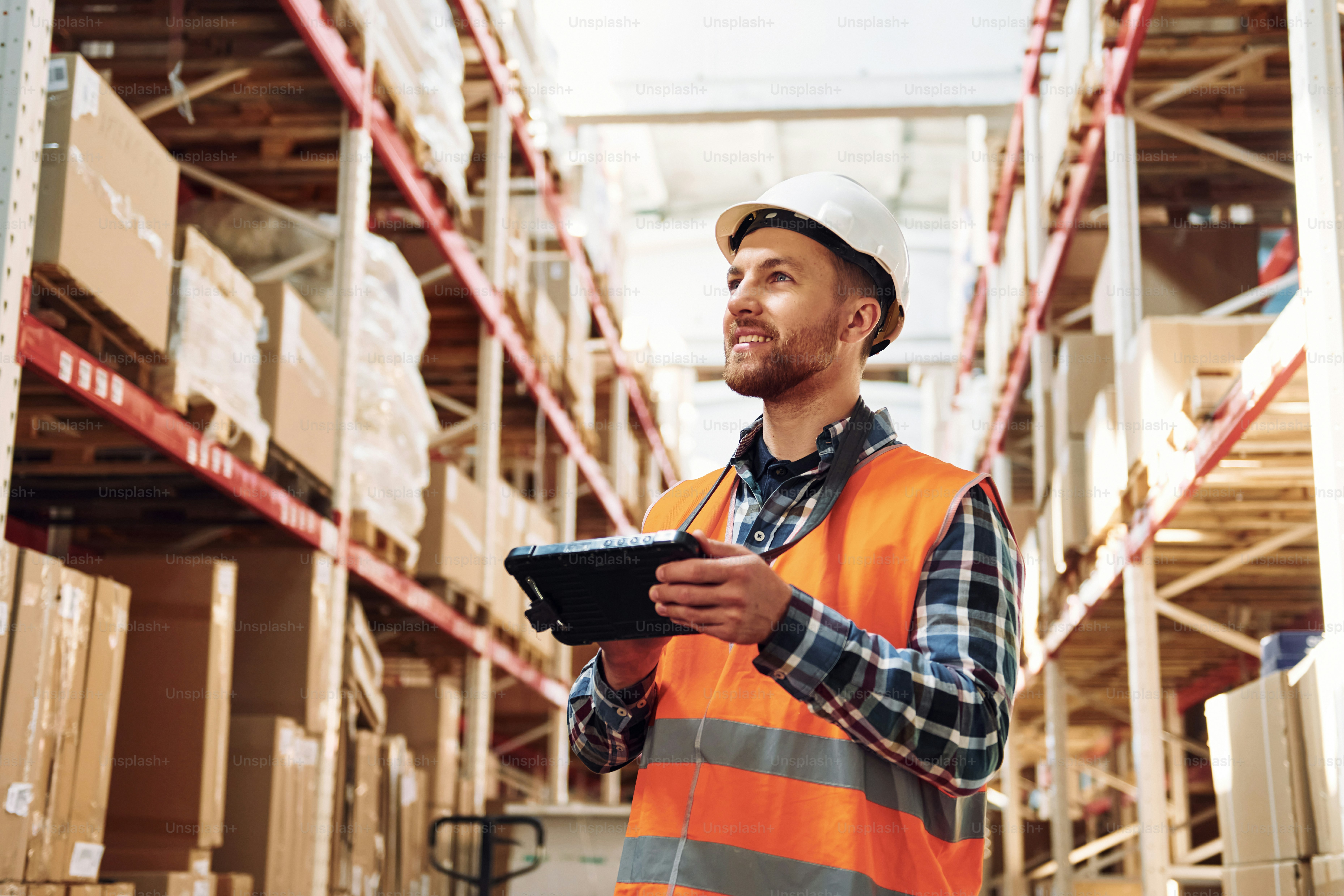 With tablet. Employee in uniform is working in the storage at daytime.