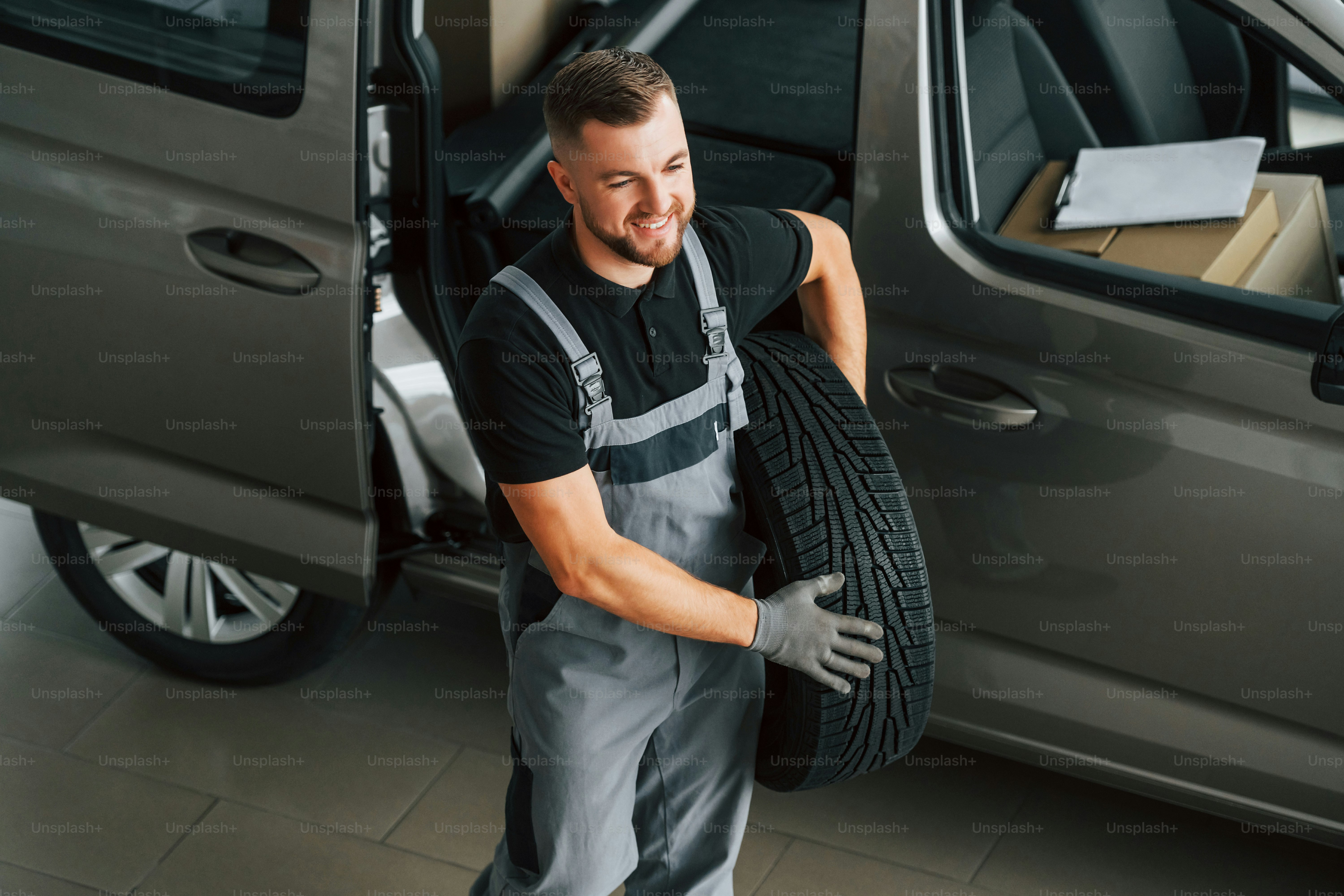 Changing tires season. Man in uniform is working in the autosalon at daytime.