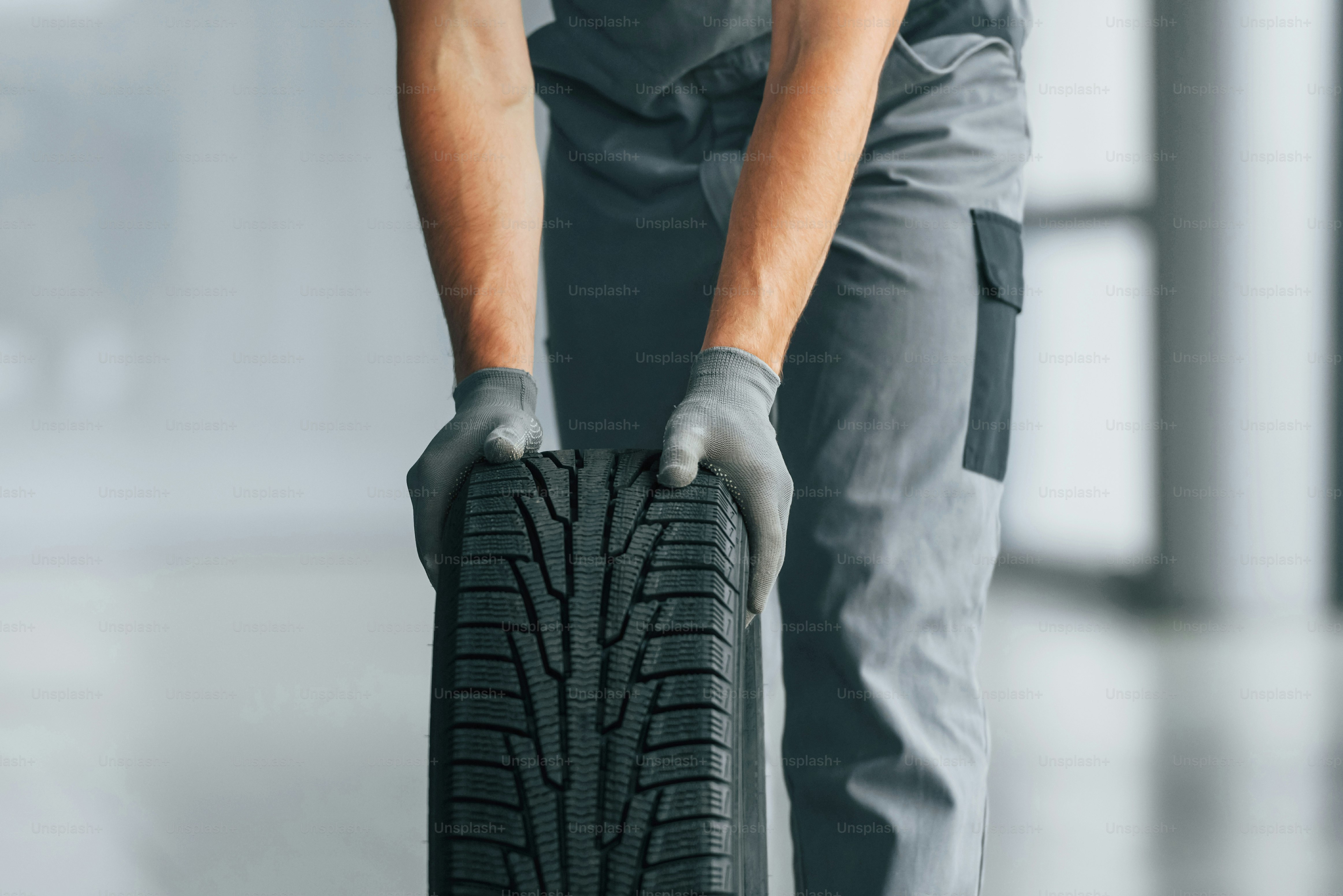 Tire on the floor. Man in uniform is working in the autosalon at daytime.