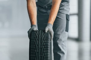 Tire on the floor. Man in uniform is working in the autosalon at daytime.