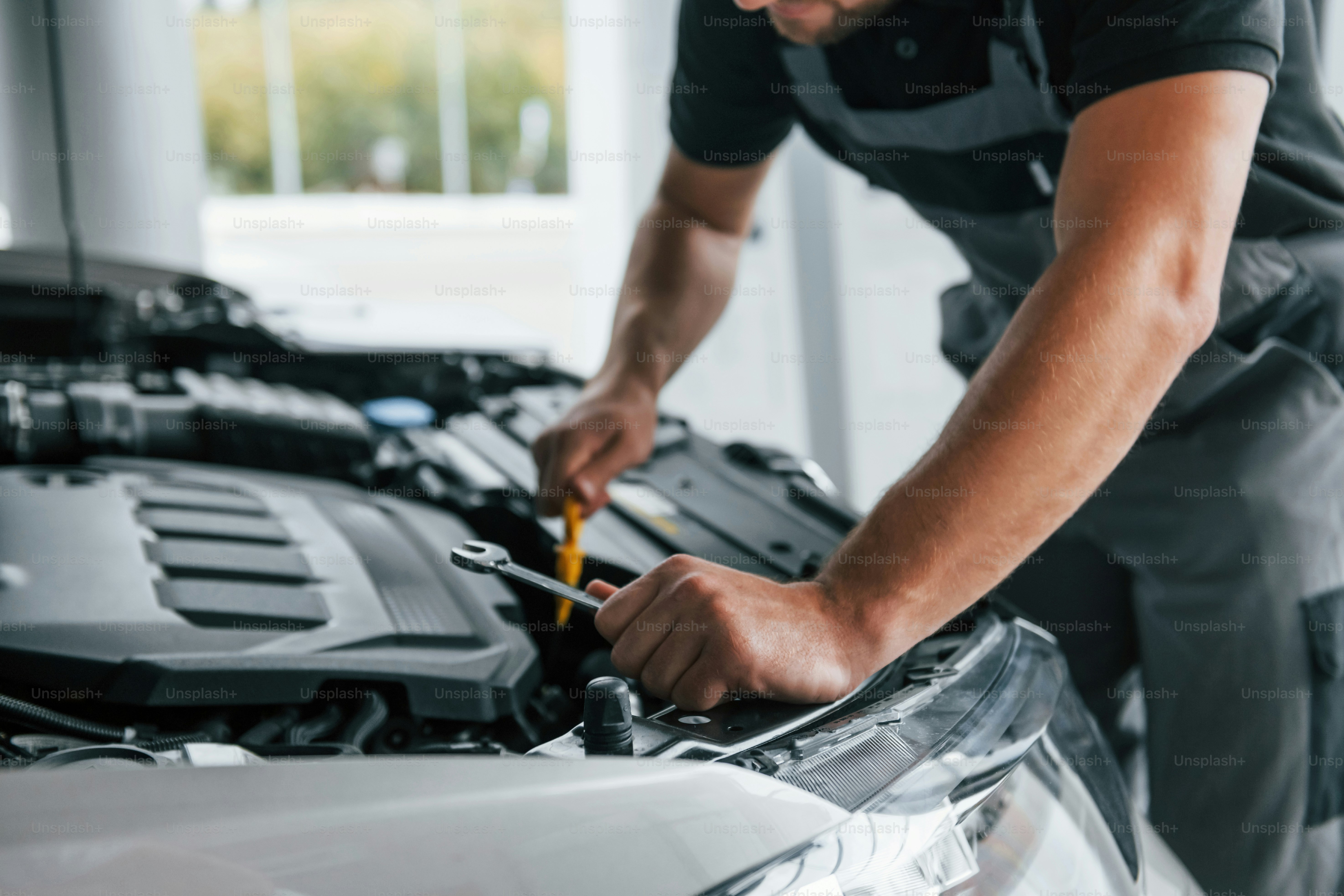 Some problems under the hood. Man in uniform is working in the autosalon at daytime.