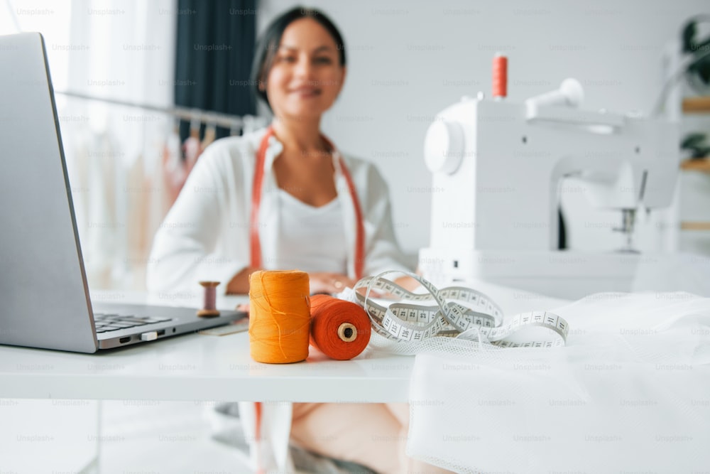 White colored sewing machine. Seamstress is in her office that is with different clothes.