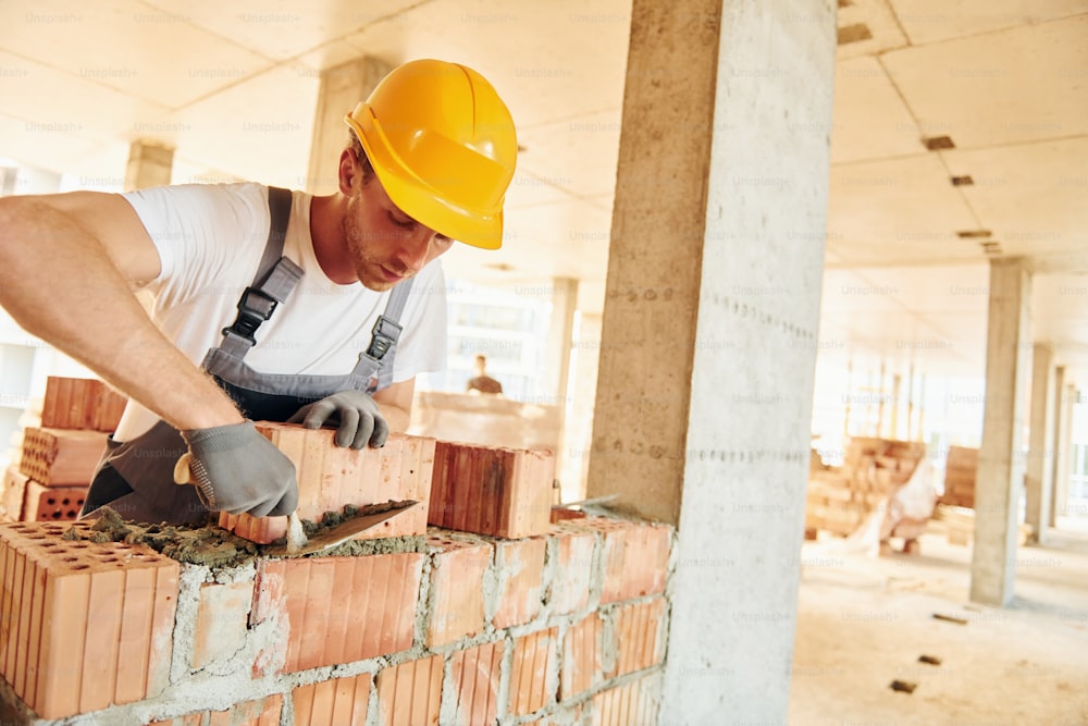 Working by using bricks. Young man in uniform at construction at daytime.