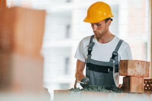 Building process. Young man working in uniform at construction at daytime.