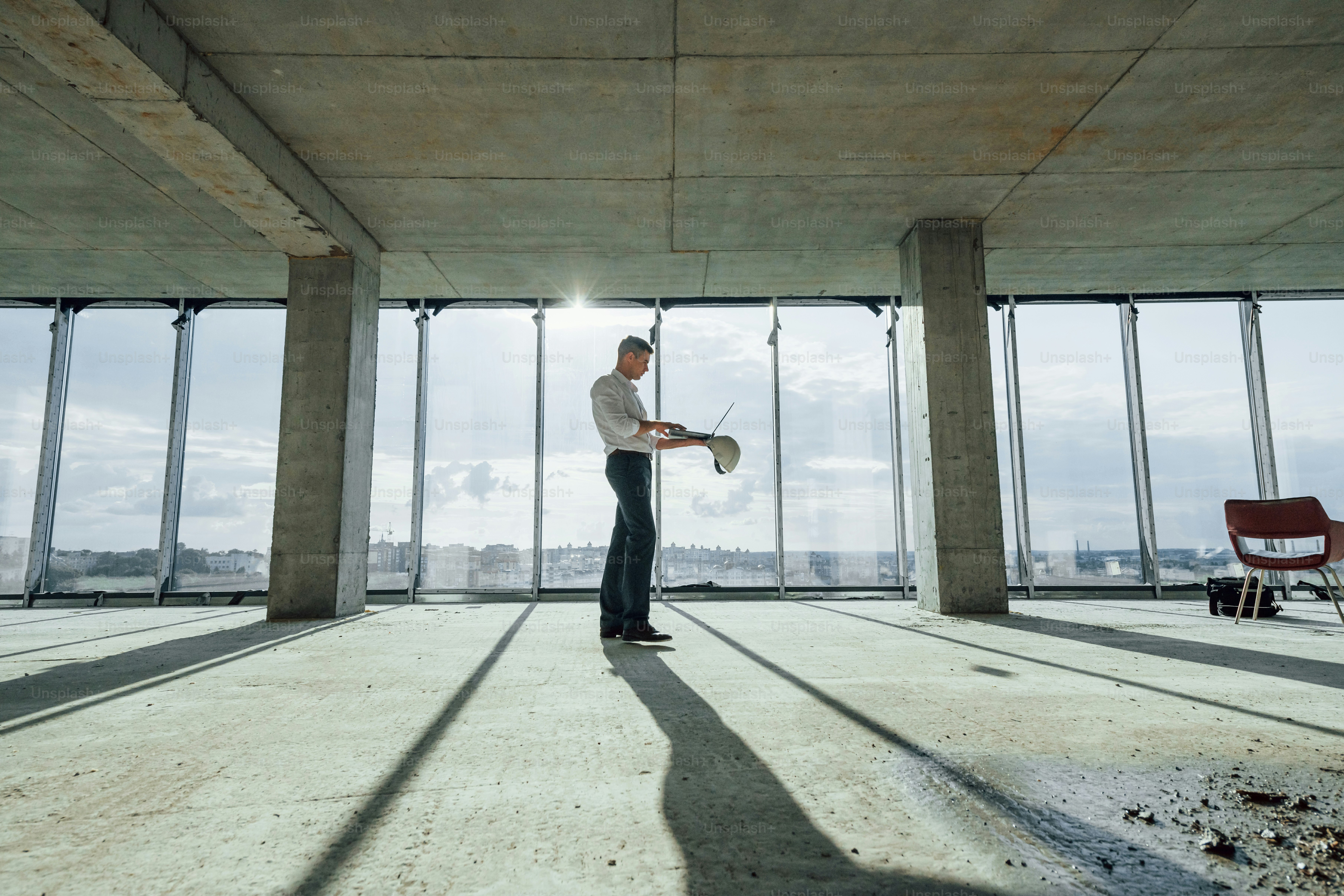 Beautiful sunlight goes through big window. Young man in formal wear is working indoors on the construction.