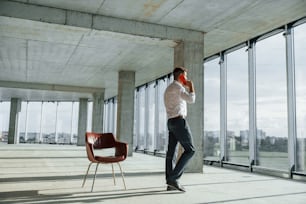 Having conversation by using phone. Young man in formal wear is working indoors on the construction.