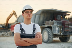 Near loading vehicle. Worker in professional uniform is on the borrow pit at daytime.