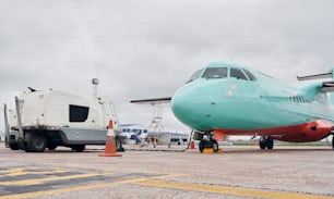 Vehicle nearby. Turboprop aircraft parked on the runway at daytime.