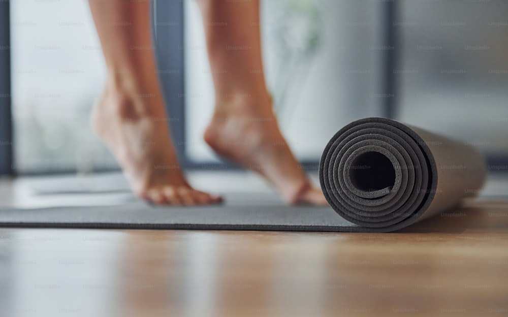 Vista focada de perto no tapete. Mulher jovem em trajes esportivos e com corpo magro tem dia de yoga fitness dentro de casa.
