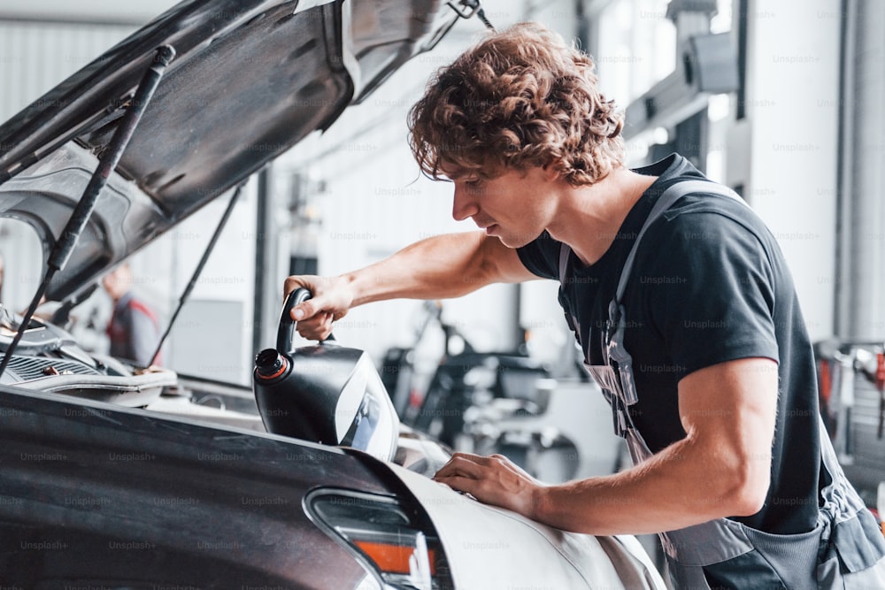 Cambio de aceite. Un hombre adulto con uniforme de color gris trabaja en el salón del automóvil.