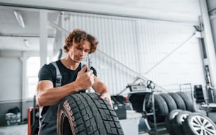 Fonctionne avec pneu. Un homme adulte en uniforme de couleur grise est dans le salon de l’automobile.