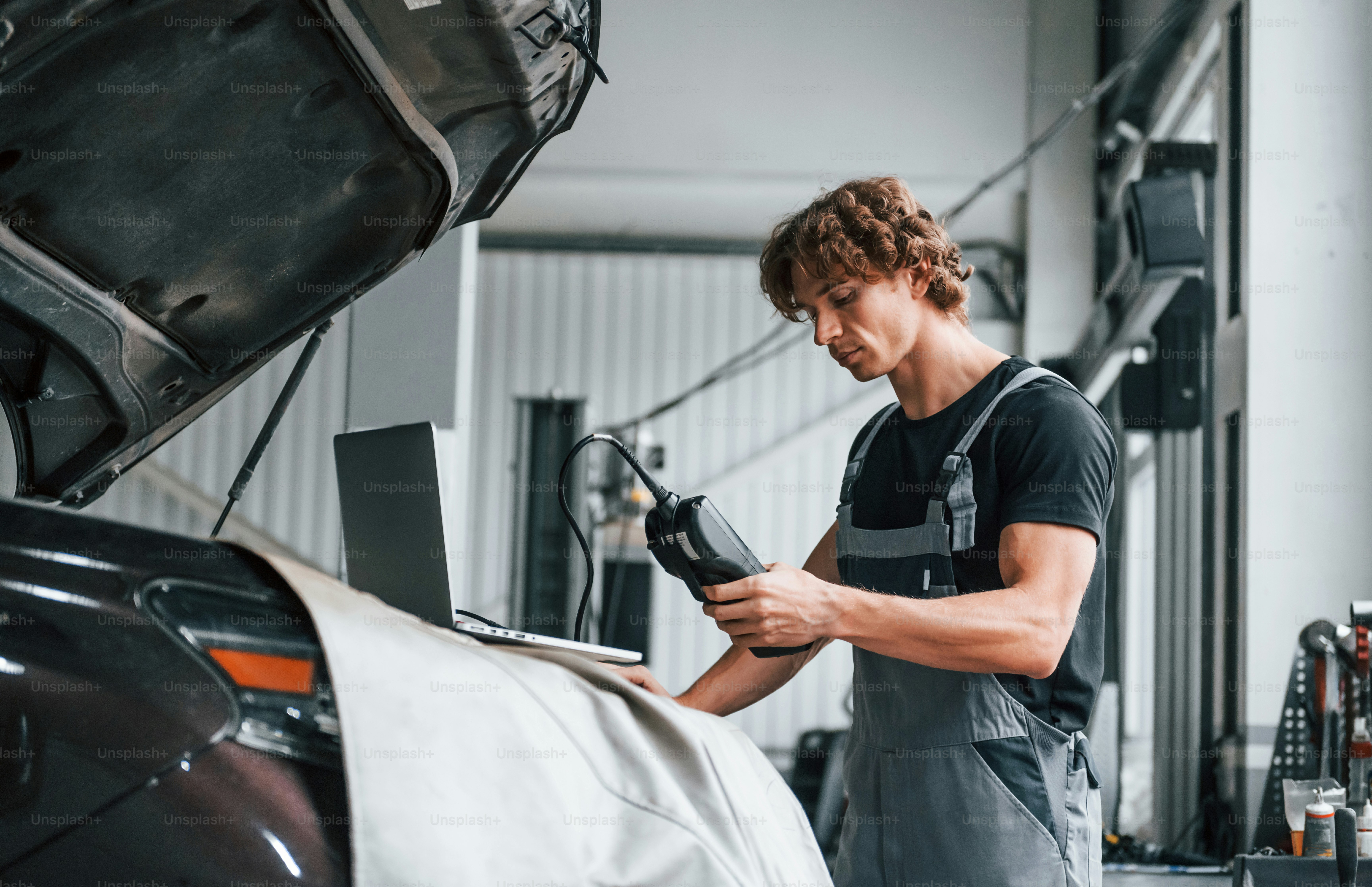 Special tool for testing characteristics. Adult man in grey colored uniform works in the automobile salon.