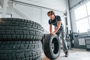 Rolls the tire. Adult man in grey colored uniform works in the automobile salon.