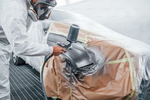 Lavori di verniciatura in corso. Riparatore di automobili caucasico in uniforme lavora in garage.