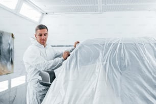 Caucasian automobile repairman in uniform works in garage.