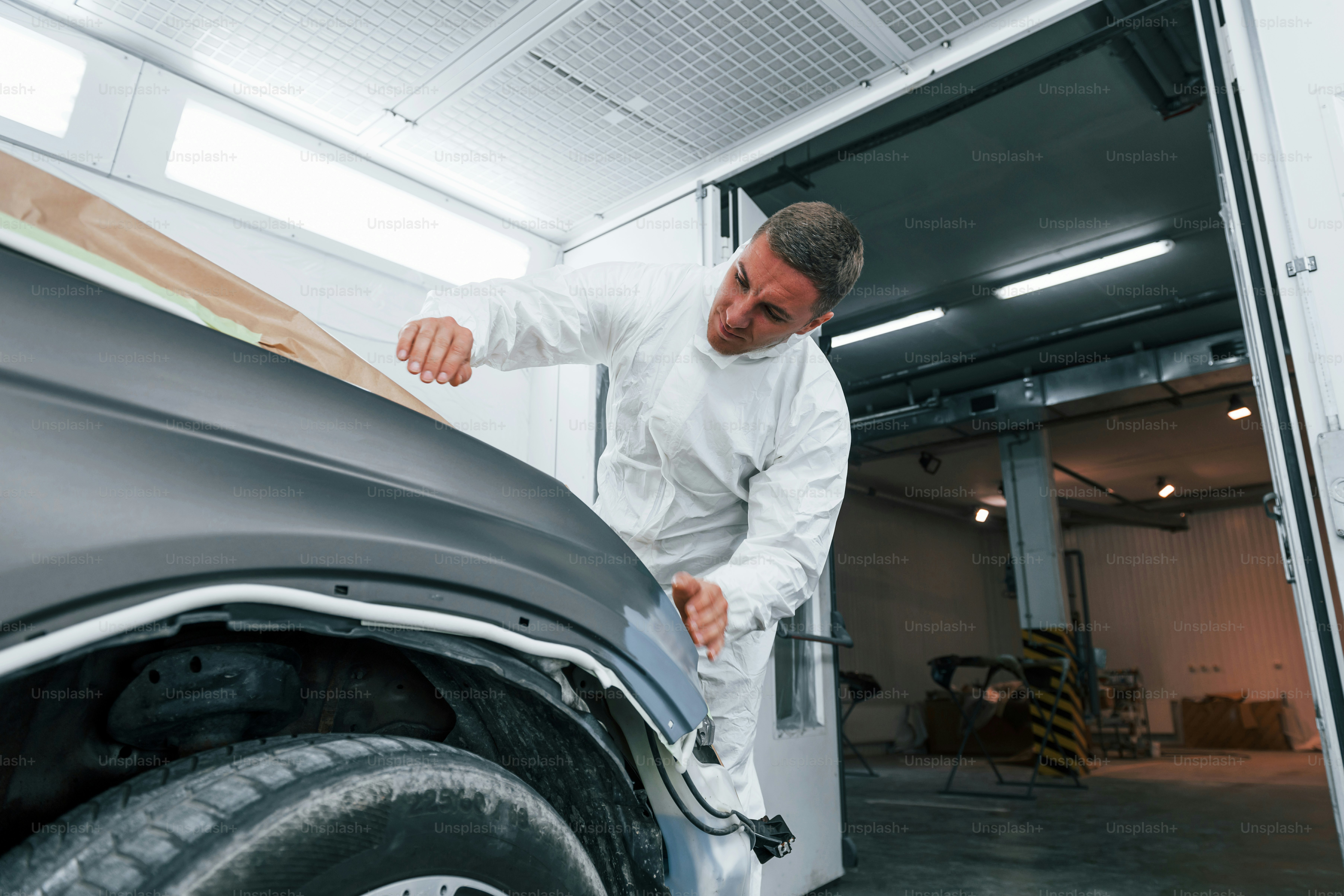 Covering car by brown cloth. Caucasian automobile repairman in uniform works in garage.