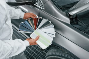 Contiene carte con colori diversi. Riparatore di automobili caucasico in uniforme lavora in garage.